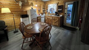 A wooden cabin interior with a dining table, chairs, a refrigerator, a stove, and a kitchen counter.