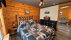A wooden-paneled room with a bed, a dresser, and a wall-mounted lamp. - Cozy, pet-friendly, 2-bedroom cabin in beautiful Palmer, Alaska (Palmer)
