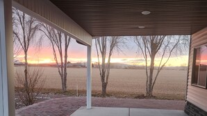 Een overdekte veranda met uitzicht op een zonsondergang boven een veld en bomen.