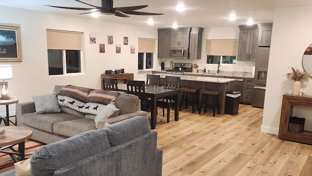 Een moderne keuken met donkere kastjes, een centraal eiland en een eethoek met houten stoelen.