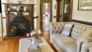 A living room with a fireplace, a beige sofa, and a coffee table with books and a vase of flowers. - Middleton House Maleny.  Picture perfect country house for small gatherings. (Witta)