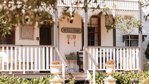 A white porch with a 'WELCOME' sign, decorative ironwork, and potted plants. - Middleton House Maleny.  Picture perfect country house for small gatherings. (Witta)
