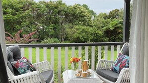A covered outdoor seating area with white wicker furniture, a small table with a pitcher and cups, and a view of a lush garden. - Middleton House Maleny.  Picture perfect country house for small gatherings. (Witta)