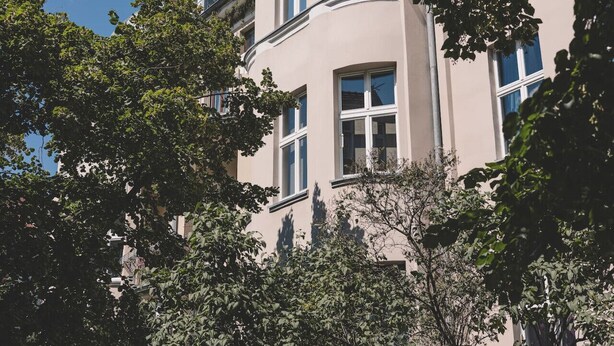 A multi-story building with a curved facade, large windows, and surrounding trees. - Arcano | Studio dla Dwojga | Przytulne wnętrze (Bydgoszcz)