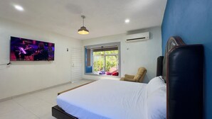 Un dormitorio con cama, televisor montado en la pared, equipo de aire acondicionado y ventana con vista a la vegetación.