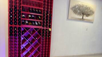 Uma estante para vinho tinto com várias prateleiras, um quadro de uma árvore na parede e um chão em azulejos.