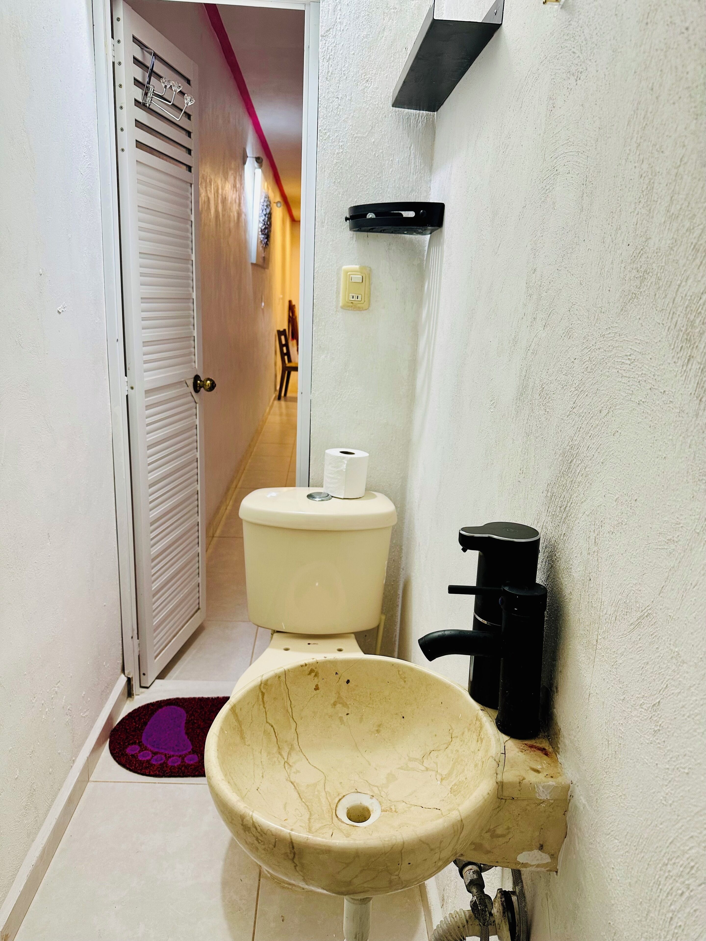A bathroom with a white toilet, a beige sink, and a black soap dispenser.