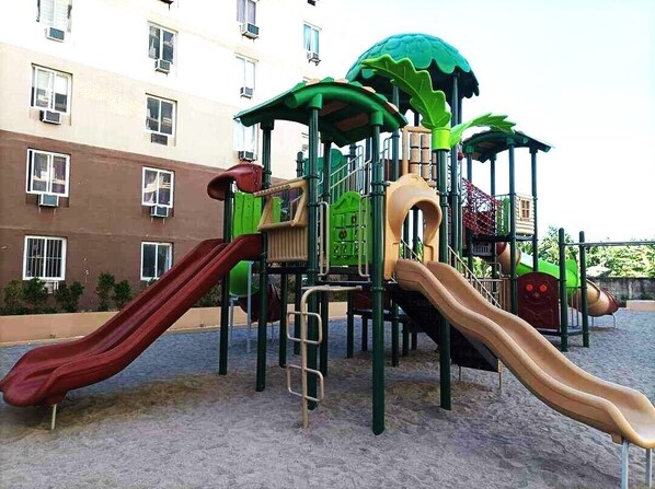 A playground with multiple slides and climbing structures, surrounded by a building with multiple windows. - Cozy Mactan Stay: Top Amenities Near Beaches & Attractions! (Lapu-Lapu City)