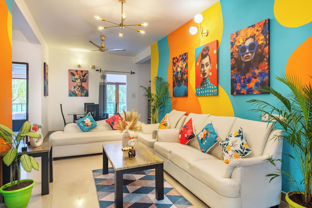 Una sala de estar moderna con un sofá blanco, una mesa de centro y obras de arte coloridas en las paredes.