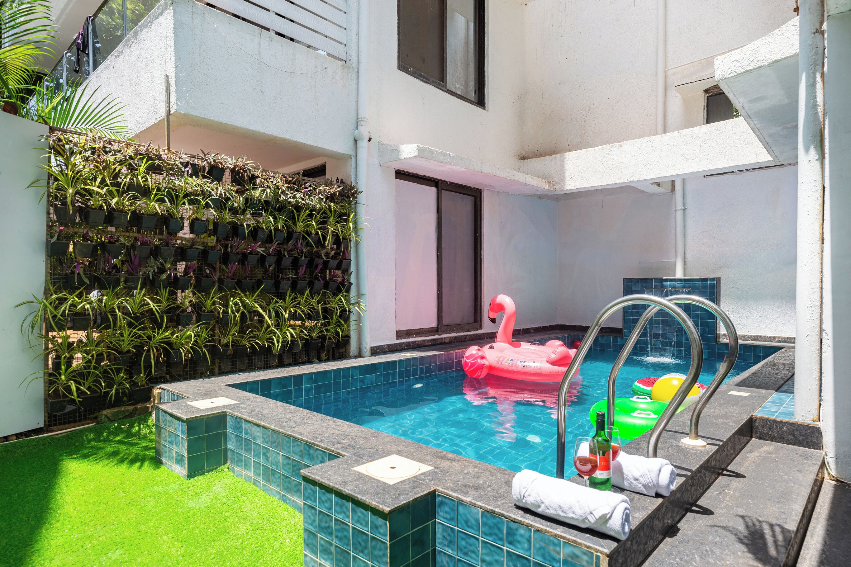 A swimming pool with a pink flamingo float, a green inflatable pool toy, and a bottle of wine on the edge.