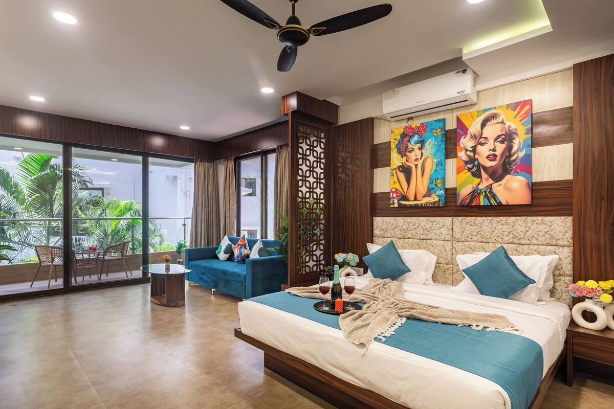Una habitación de hotel moderna con balcón, cama con ropa de cama azul, ventilador de techo y obras de arte en la pared.