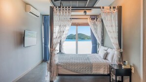 Un dormitorio con cama, cortinas, una mesita de noche y vistas al mar.