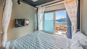 Un dormitorio con cama, televisión y balcón con vista al mar.