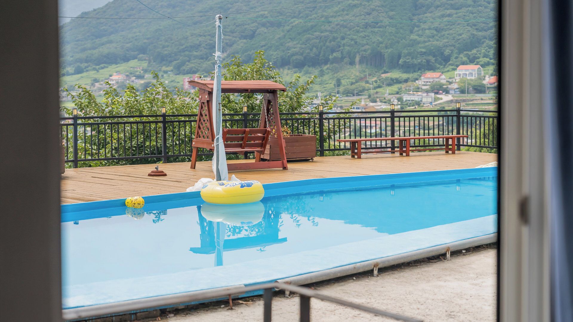 Une piscine avec une terrasse en bois, une balançoire en bois et un banc.