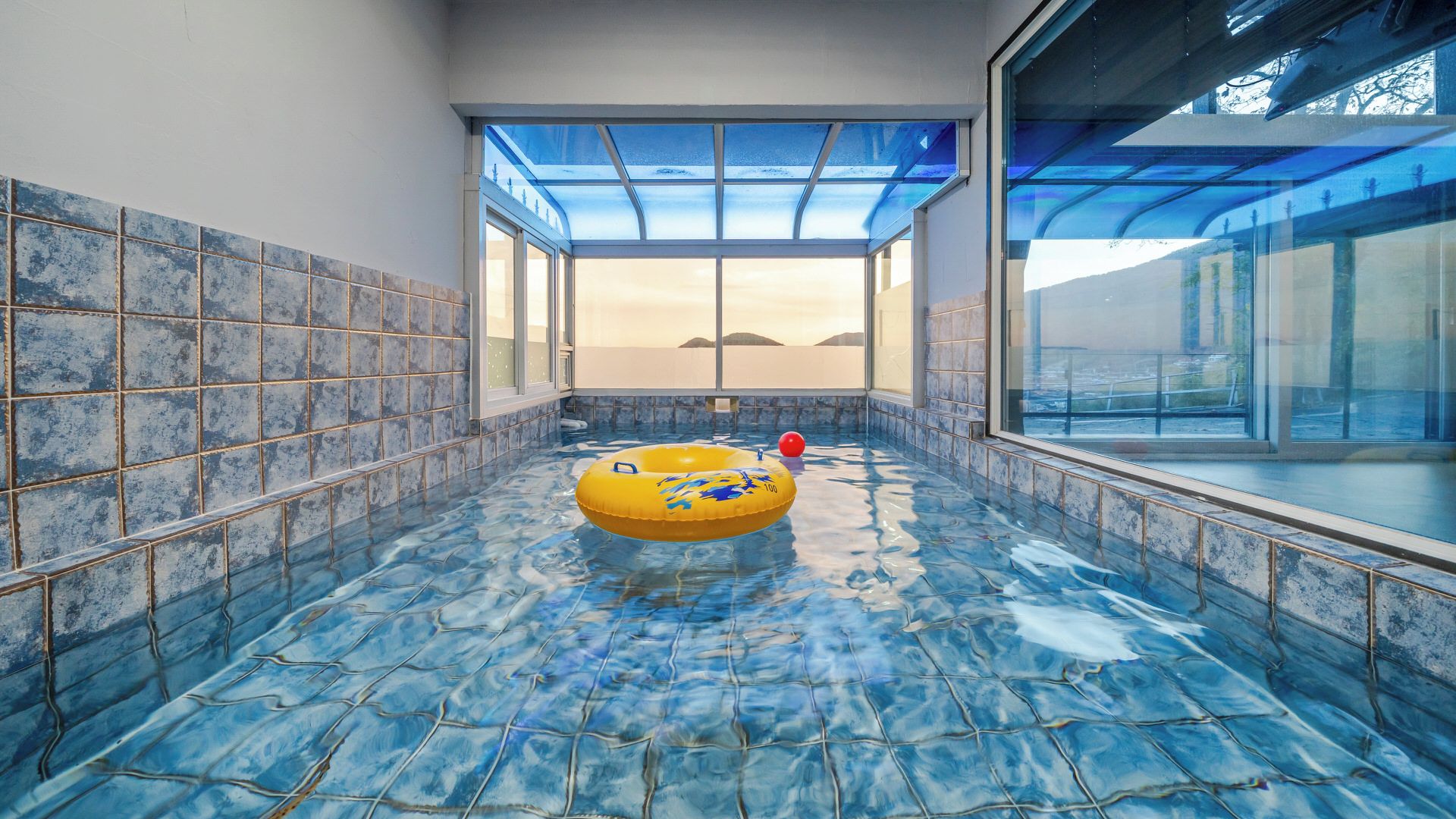A swimming pool with a glass ceiling, a yellow inflatable ring, and a red ball.