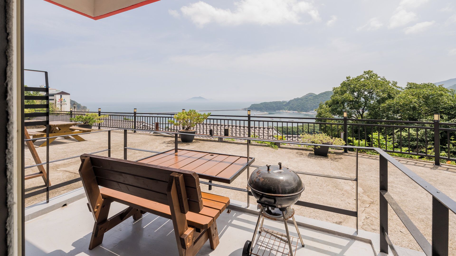 Un balcone con panchina e tavolo in legno, con vista panoramica sul mare e le colline.