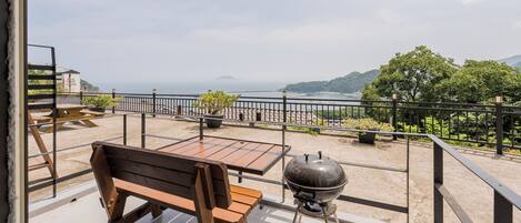 Un balcone con panchina e tavolo in legno, con vista panoramica sul mare e le colline.