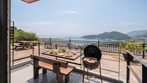 A balcony with a grill, picnic table, and benches overlooking a coastal view. - Namhae Aria Spa Pension (Namhae)