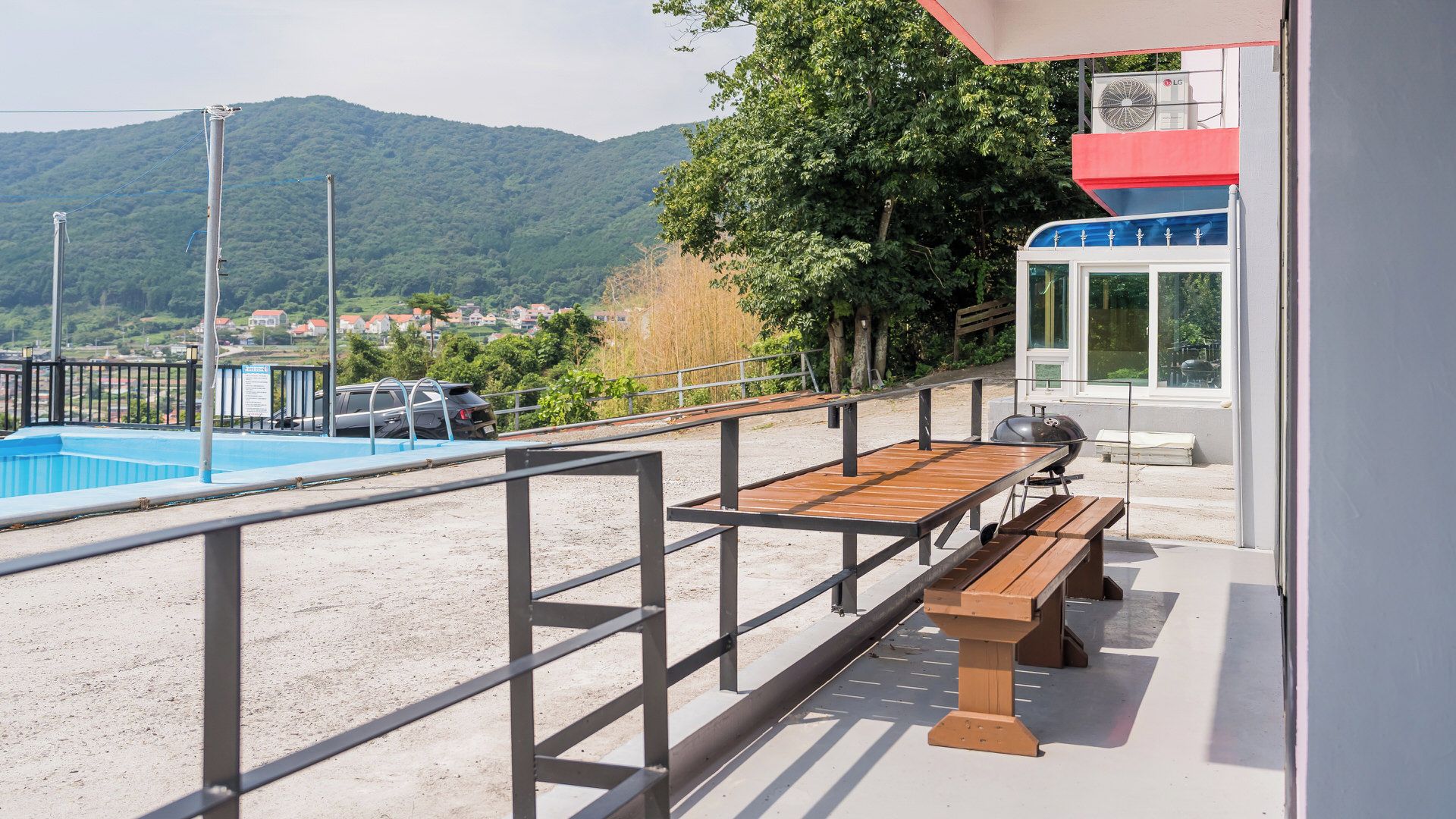 A poolside area with a wooden bench and a grill, overlooking a mountainous landscape.