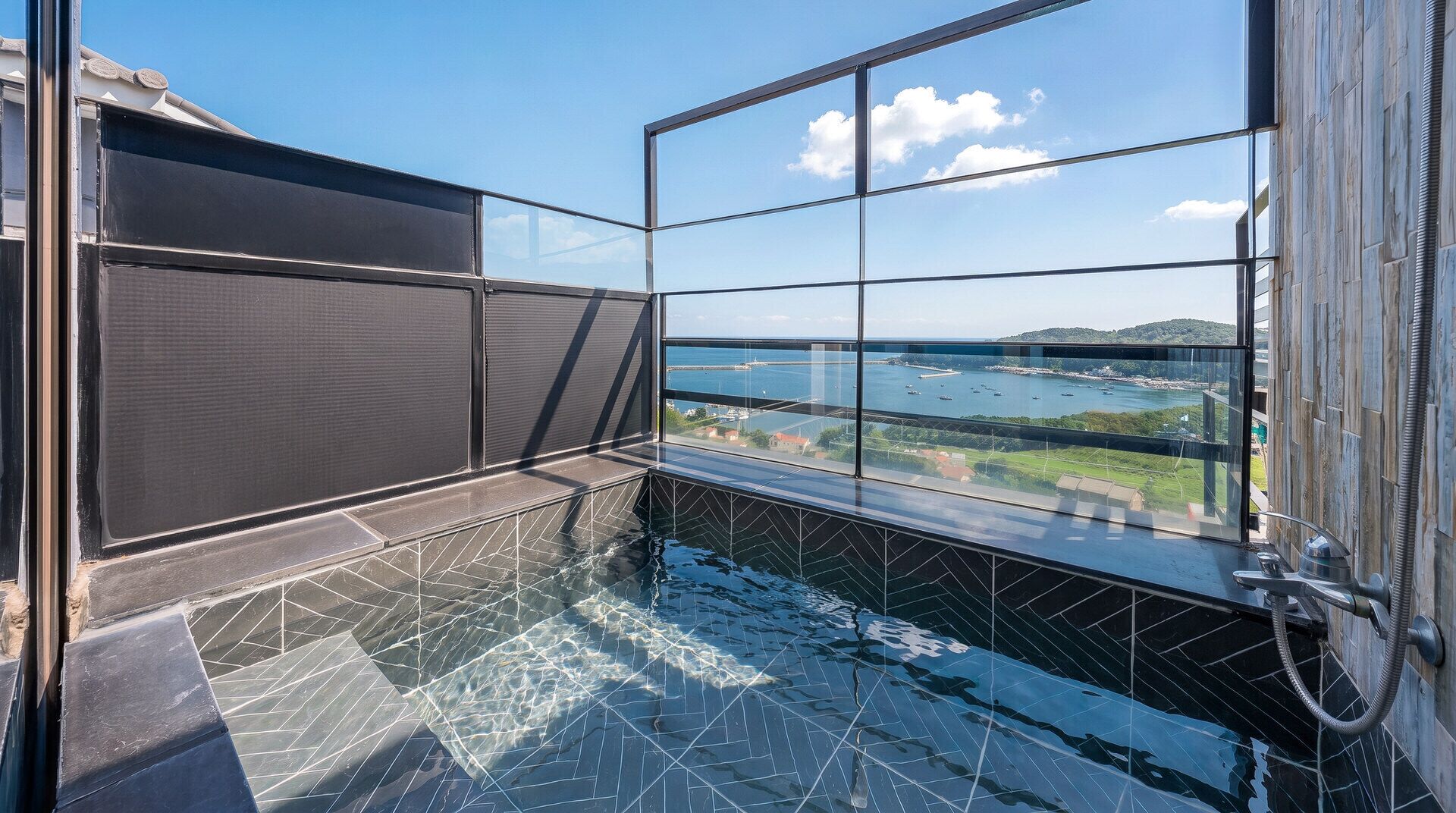 A balcony with a glass enclosure overlooking a body of water and a distant landscape.