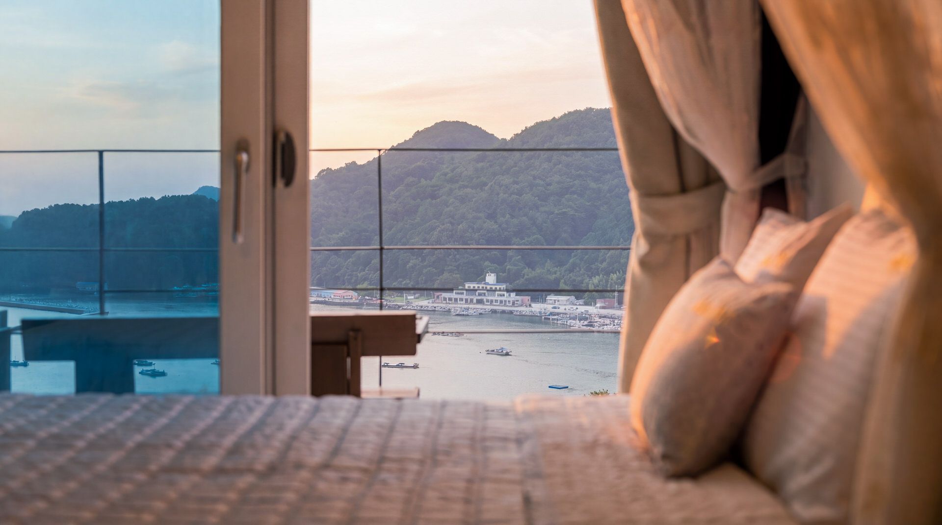A hotel room with a view of a harbor, boats, and a distant mountain.