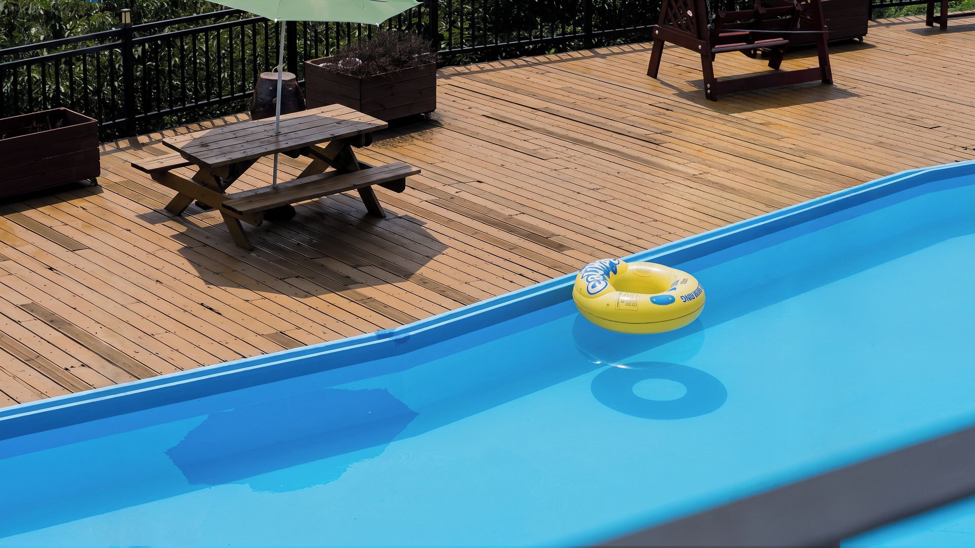 Een houten terras met een zwembad, een gele opblaasbare ring en een picknicktafel.
