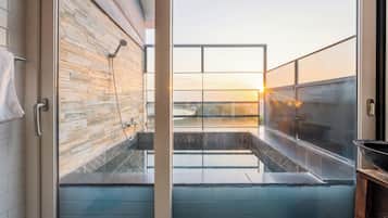 Ein modernes Badezimmer mit Dusche, Blick auf den Sonnenuntergang und einem großen Fenster.