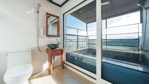 A modern bathroom with a toilet, sink, and a large glass door leading to a balcony. - Namhae Aria Spa Pension (Namhae)