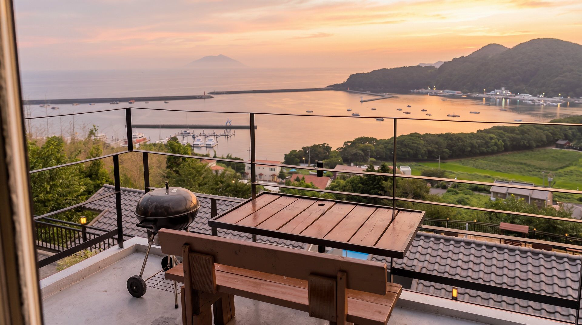 A balcony with a table and chairs, overlooking a marina with boats and a hilly landscape.