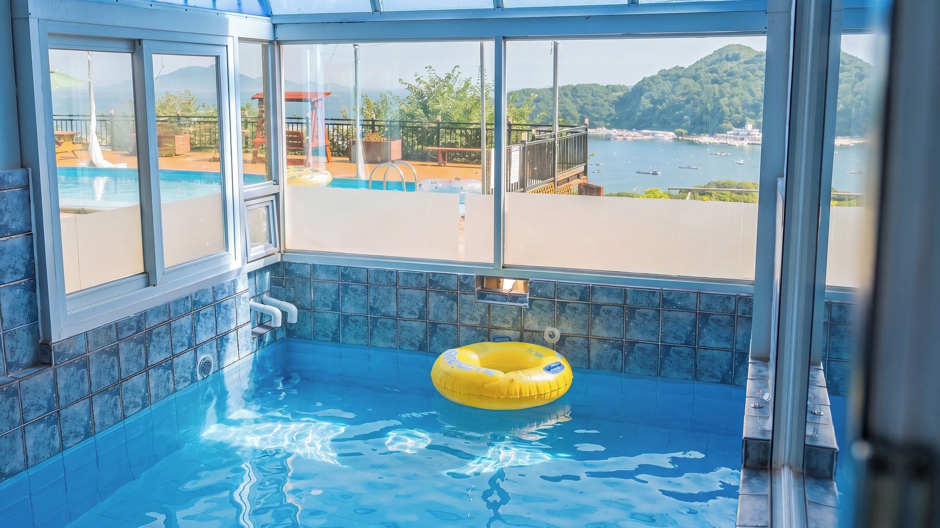 An indoor swimming pool with a view of a body of water and hills.