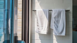Baño con dos toallas colgadas en un perchero frente a una pared azulejada.