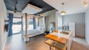 A modern bedroom with a bed, a bedside table, a nightstand, a window with curtains, and a view of the outdoors. - Namhae Aria Spa Pension (Namhae)