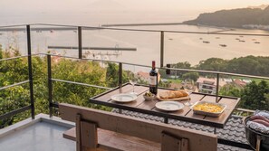 A balcony with a table set for a meal, overlooking a body of water and a distant shoreline. - Namhae Aria Spa Pension (Namhae)