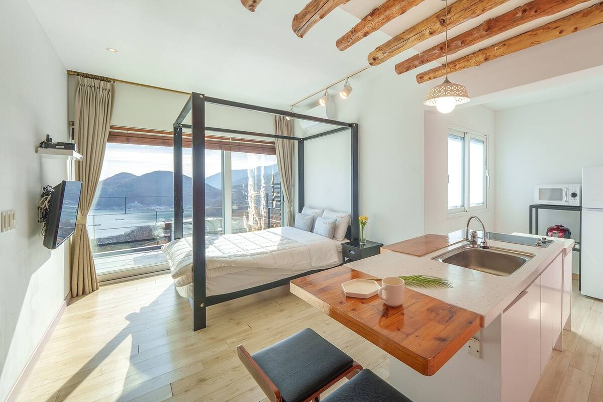 A modern bedroom with a large bed, a view of the sea, and a wooden ceiling.