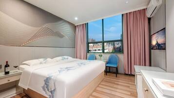 A modern hotel room with a large bed, a desk, and a chair. There is a window with a view of buildings and a cityscape.