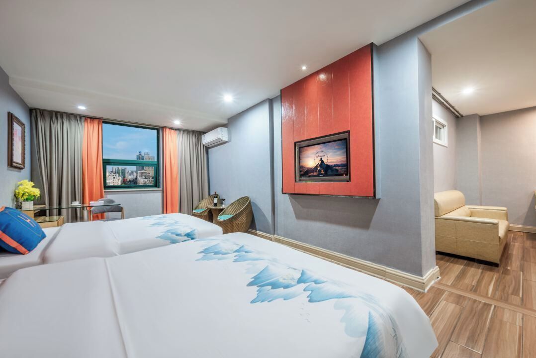 A hotel room with two beds, a city view, a mounted picture, a chair, and a small table with a vase.
