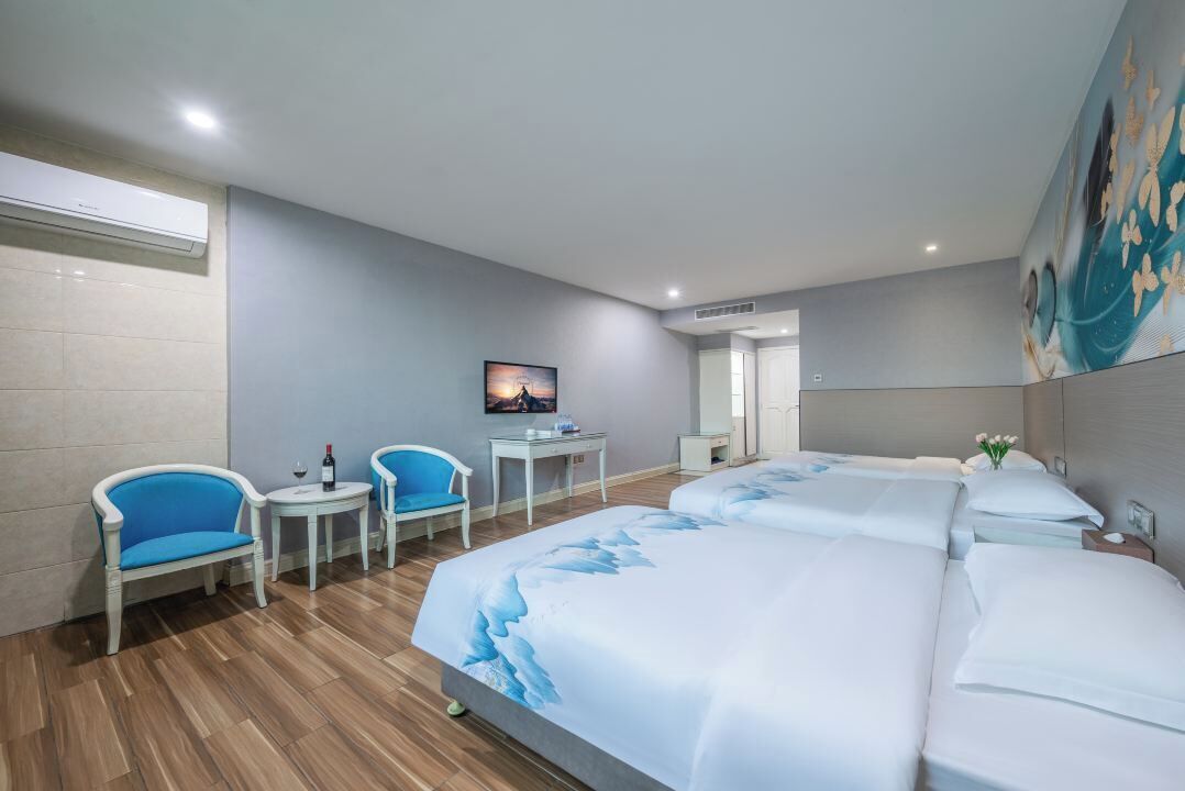 A hotel room with two beds, a desk, two chairs, a TV, and a bathroom.