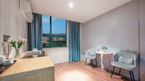 A modern hotel room with a wooden floor, a small kitchen area, a dining table with chairs, and a large window offering a city view. - xingduhuadujiudian (Quanzhou)