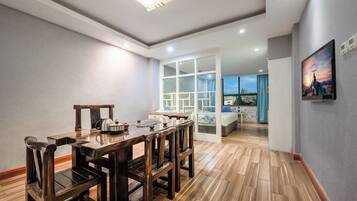 Una habitación de hotel moderna con una mesa de comedor de madera, sillas y vistas de la ciudad a través de amplias ventanas.