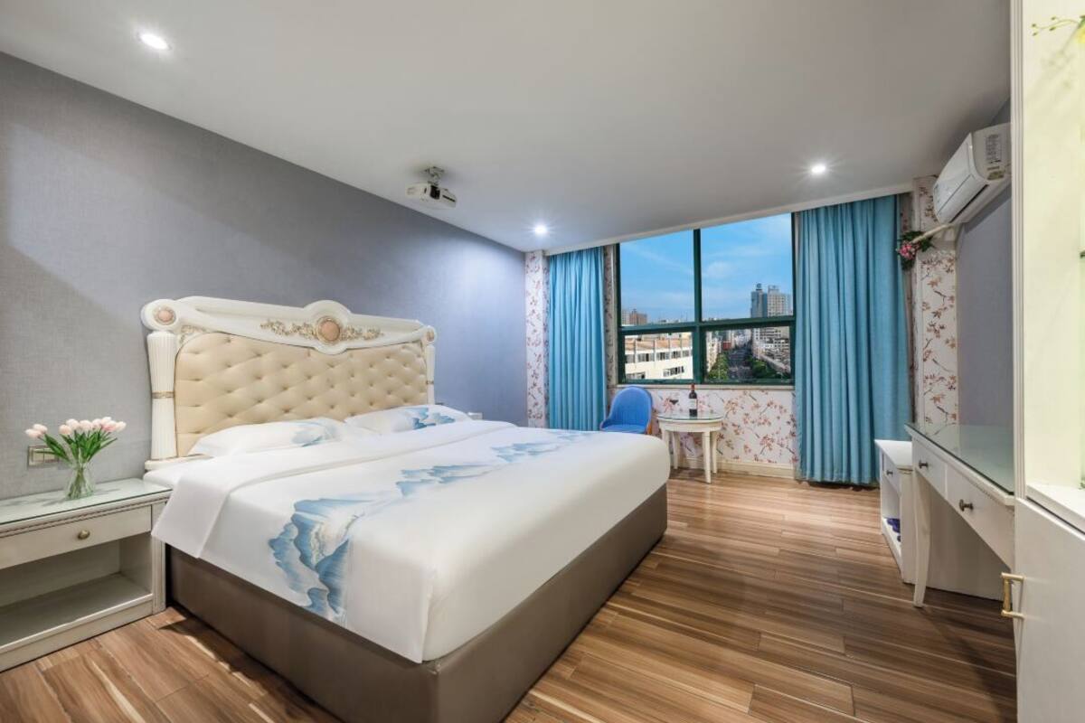Une chambre d’hôtel avec un grand lit, un petit bureau, une chaise et une vue sur la ville grâce à de grandes fenêtres.