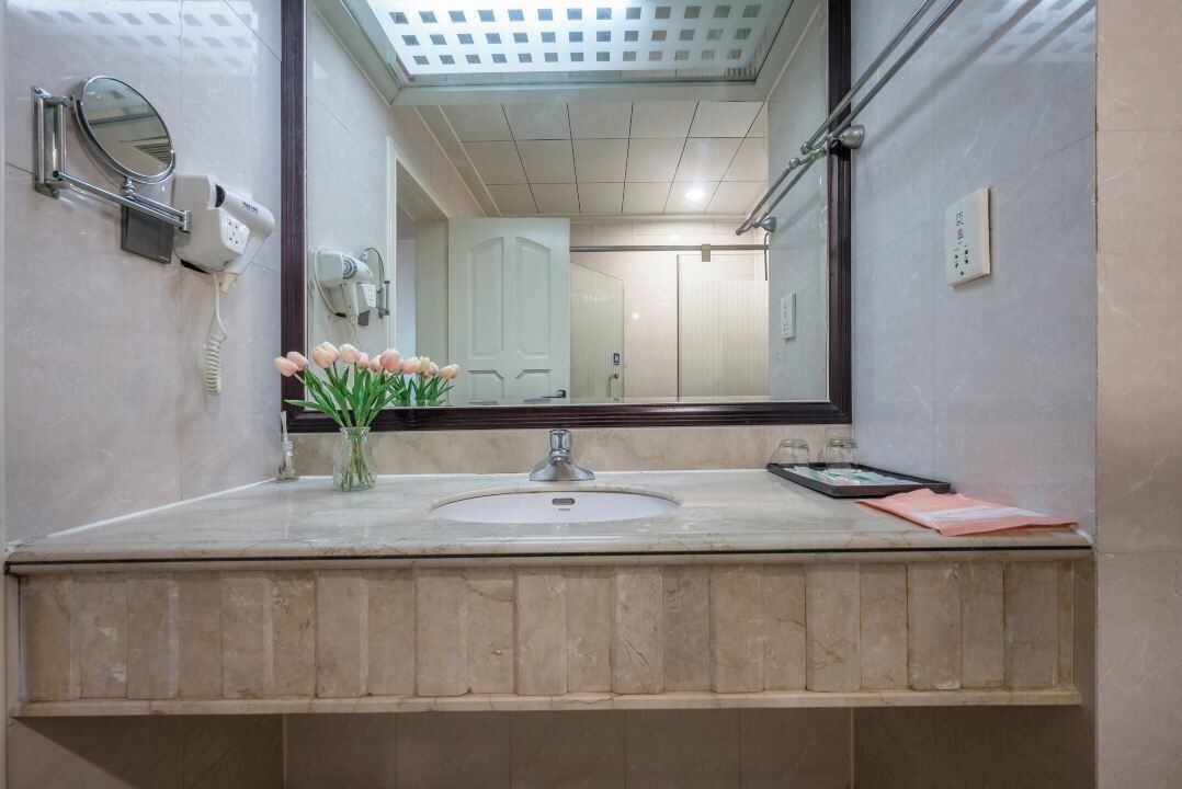 A bathroom with a sink, mirror, hairdryer, and a vase with flowers.