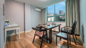 A modern room with a dining table, two chairs, a small desk, and a window with a city view. - xingduhuadujiudian (Quanzhou)