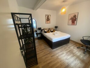 Un dormitorio bien iluminado con una cama, mesita de noche, lámpara y dos obras de arte colgadas en la pared.