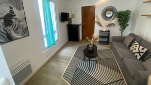 Un saló amb una taula de cafè amb ratlles negres i blanques, un sofà gris, un televisor a la paret i una porta que condueix a una altra habitació.