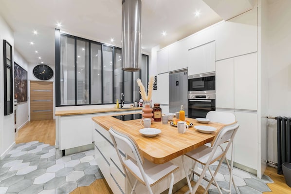 A modern kitchen with white cabinets, a wooden island, stainless steel appliances, and a large window.