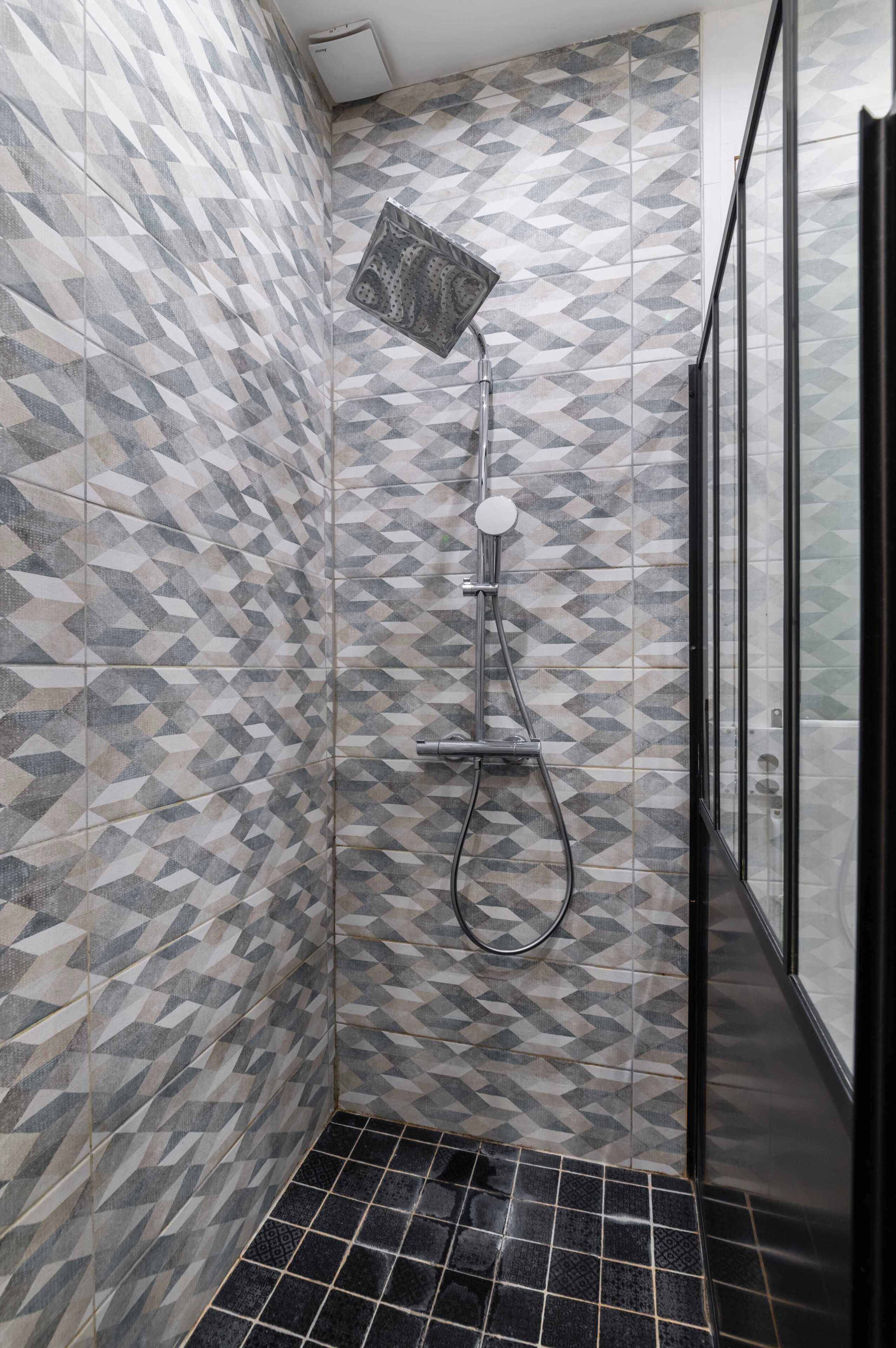 A shower with a geometric tile pattern, a handheld showerhead, and a black tiled floor.