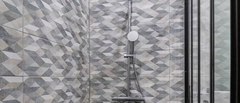 Une douche avec un carrelage aux motifs géométriques, une douchette à main et un sol carrelé de couleur noire.
