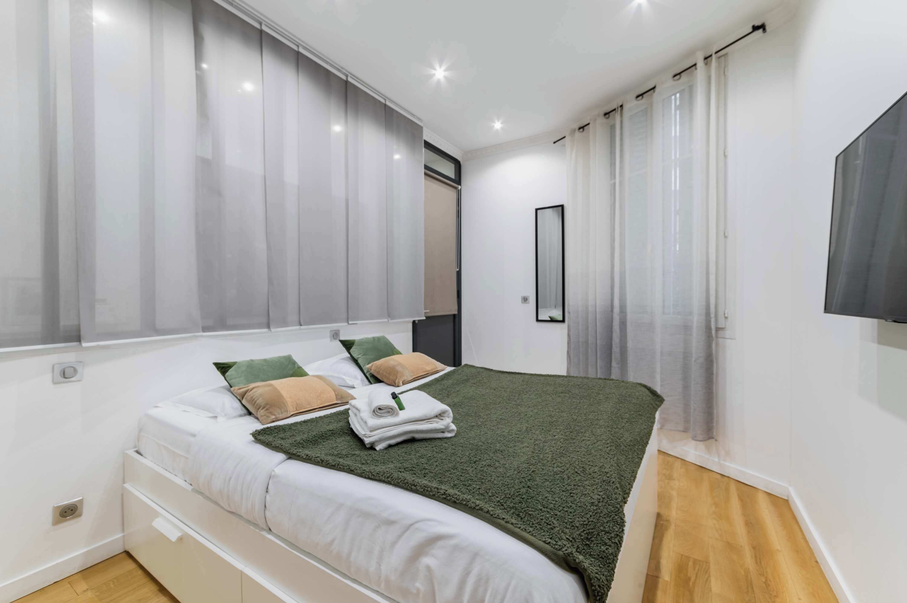 Un dormitorio moderno con cama, cortinas, espejo y televisor.