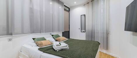 Un dormitorio moderno con cama, cortinas, espejo y televisor.