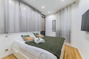 A modern bedroom with a bed, curtains, a mirror, and a TV.